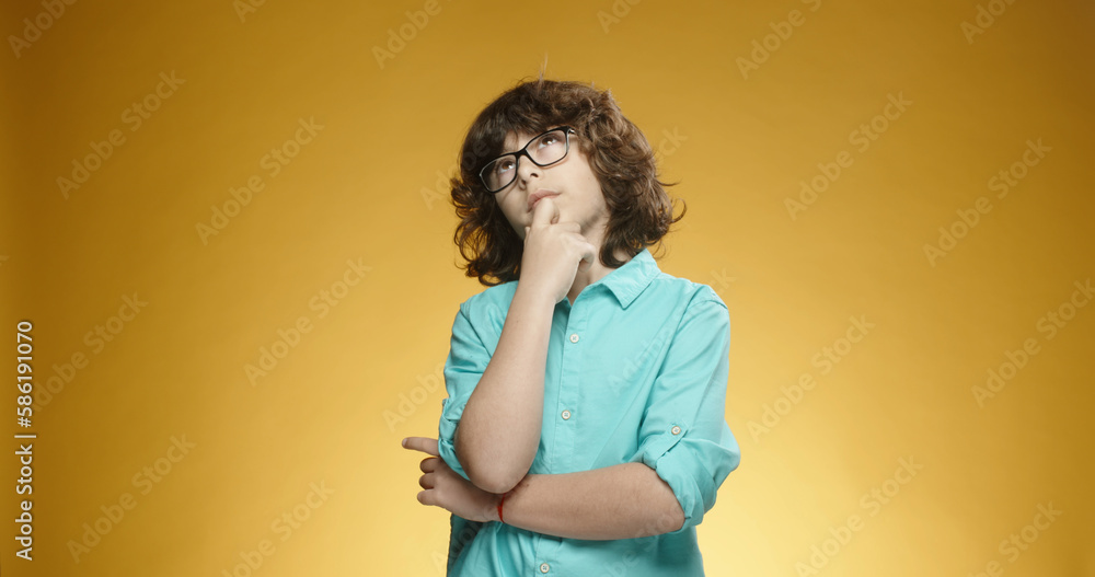 Cute caucasian boy in blue shirt and glasses looking at camera and thinking about something, isolated on yellow background - emoticons concept close up Cute caucasian boy in blue shirt and glasses looking at camera and thinking about something, isolated on yellow background - emoticons concept close up