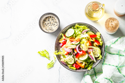 Fresh vegetable salad with green leaves, cucumber and bell pepper on white. Top view with copy space.