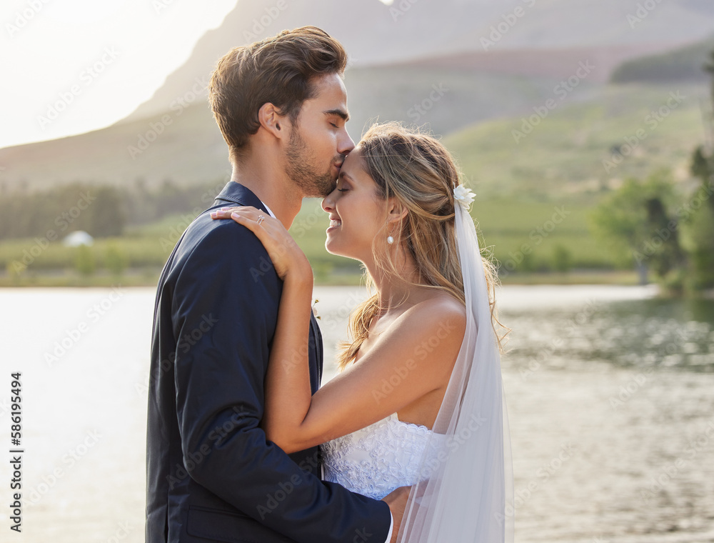 Love, wedding with a bride and groom kissing by a lake outdoor in celebration of their marriage for romance. Water, summer and kiss with a newlywed couple bonding together in tradition after ceremony