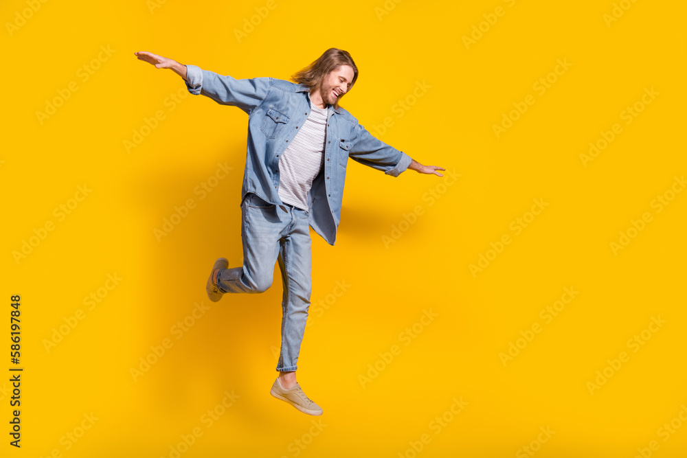 Full length photo of cool cheerful guy dressed jeans shirt jumping high emtpy space isolated yellow color background