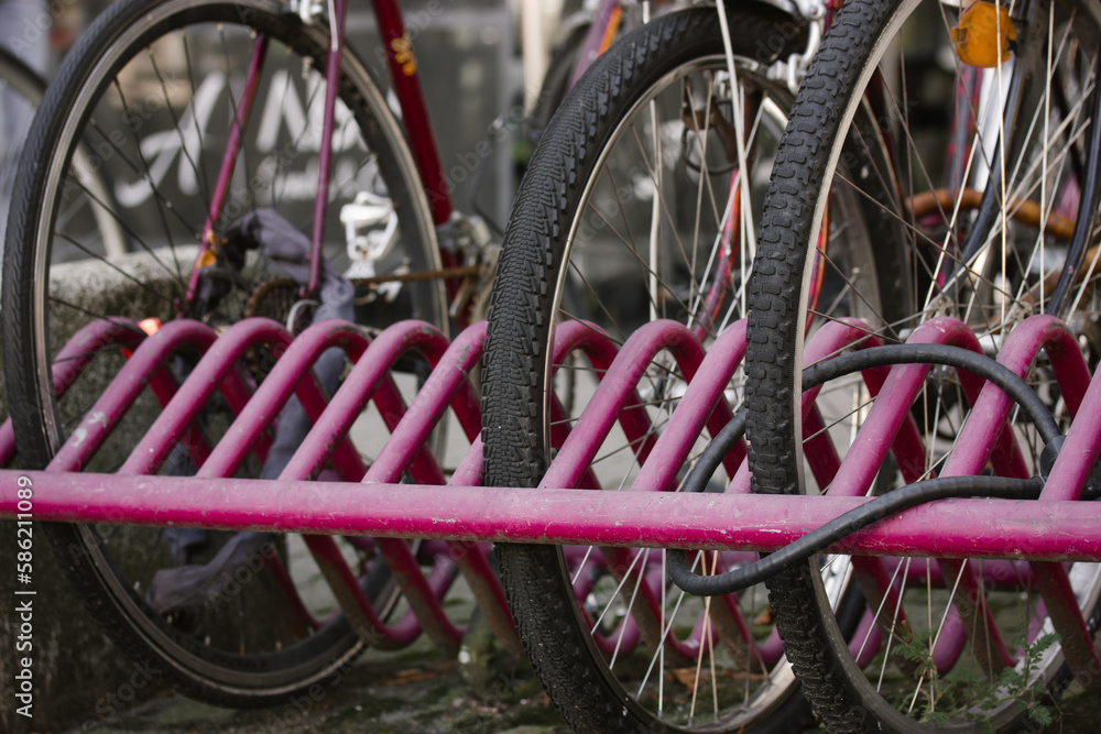 Bicycle rack. Pink bike rack in an urban environment. Reliable place to park Citybike on lock. Eco-friendly transportation. Details of bicycle tires and wheels. Bicycle locked to a metal platform. Bicycle rack. Pink bike rack in an urban environment. Reliable place to park Citybike on lock. Eco-friendly transportation. Details of bicycle tires and wheels. Bicycle locked to a metal platform.