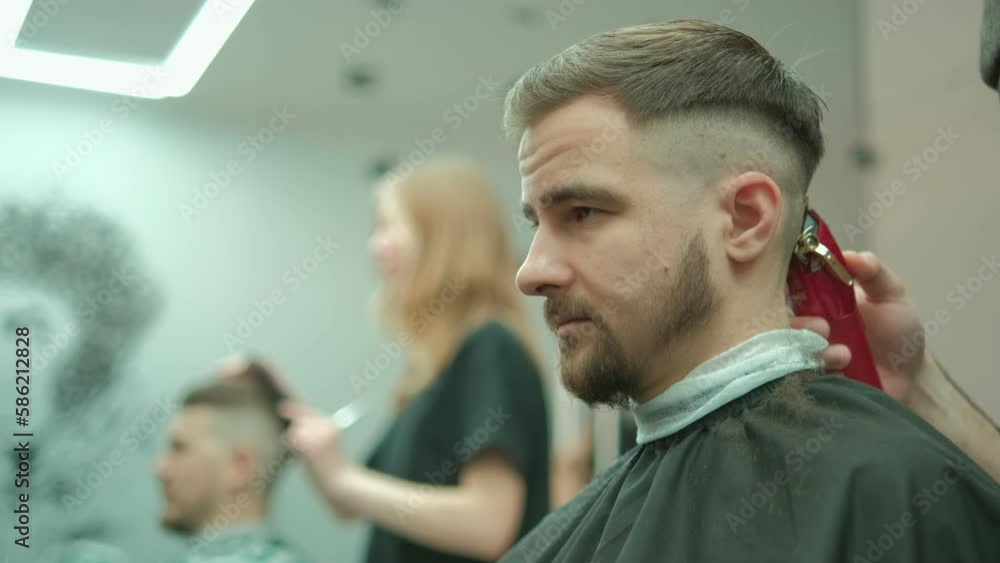 Trendy bearded barber cuts bearded man's hair with a clipper in barbershop. Men's hairstyling and hair cutting in salon. Grooming the hair with trimmer. 4K Trendy bearded barber cuts bearded man's hair with a clipper in barbershop. Men's hairstyling and hair cutting in salon. Grooming the hair with trimmer. 4K