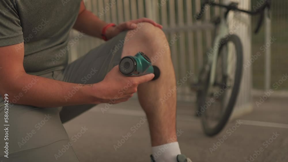 Male cyclist massages muscles and tendons with massage percussion