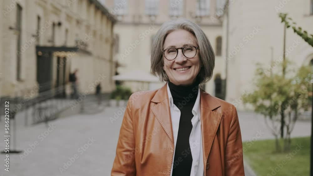 Portrait of mature smiling gray-haired businesswoman wearing eyeglasses and looking at camera. Close up face of cheerful woman with spectacles smiling outdoor. Confident beautiful entrepreneur. Portrait of mature smiling gray-haired businesswoman wearing eyeglasses and looking at camera. Close up face of cheerful woman with spectacles smiling outdoor. Confident beautiful entrepreneur.