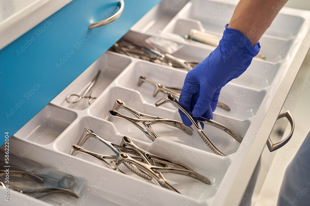 Doctor's hands wearing a disposable medical gloves holding a stainless steel nasal speculum for ENT examination over other surgery instruments