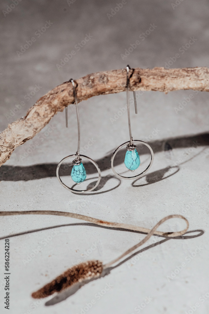 Handmade jewelry earrings made of natural turquoise and Silver on stone and modern concrete background with snag and dry flower