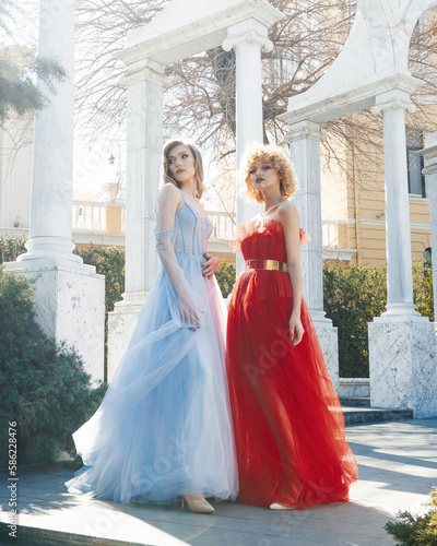 Two women in red dresses stand in front of a white columns.