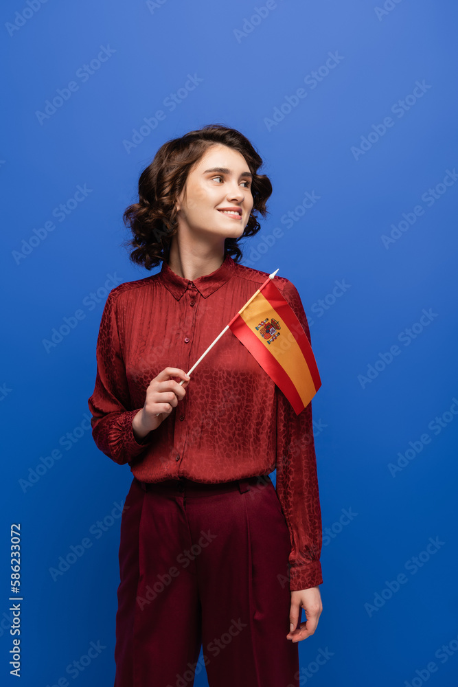happy language teacher smiling while holding flag of Spain isolated on blue. happy language teacher smiling while holding flag of Spain isolated on blue.