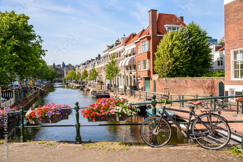 Canal lined with brick row houses on a sunny summer day. A bicycle chained to a bridge railing is in foreground.