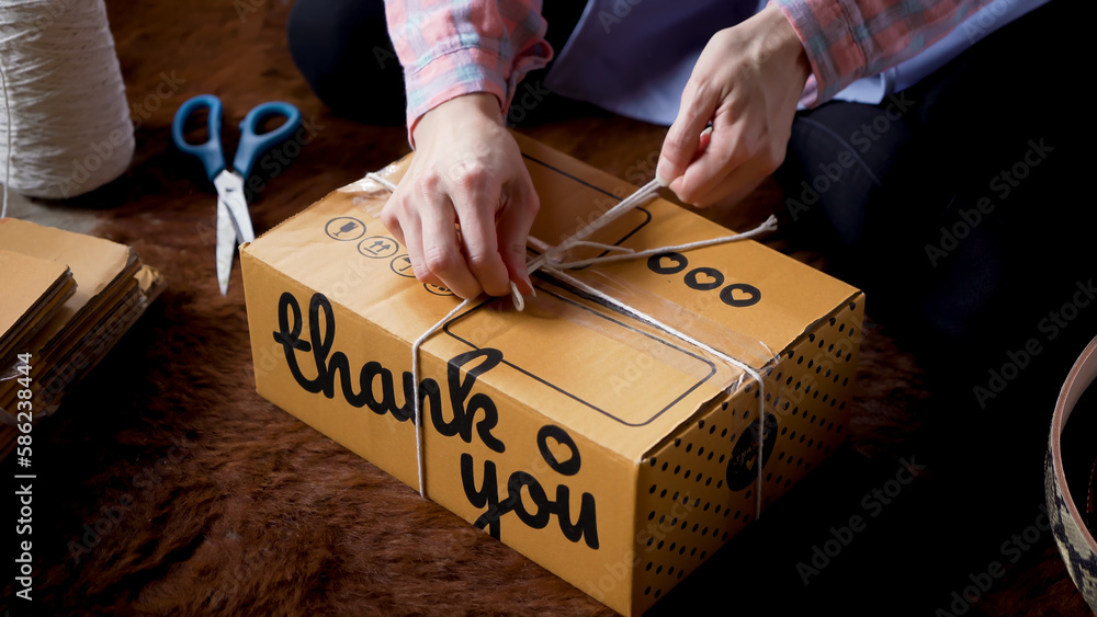 Obraz premium Close-up parcel box for pack of brown, big box, who was being hit by two hands, used white rope bind package tightly, before bringing parcel box with contents inside box be delivered customer.