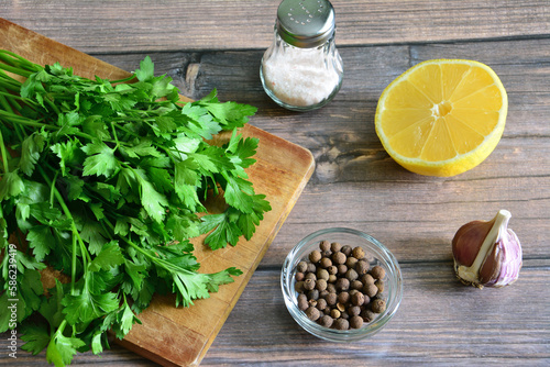 A cutting board with chopped parsley, lemon and salt shaker on wooden background 