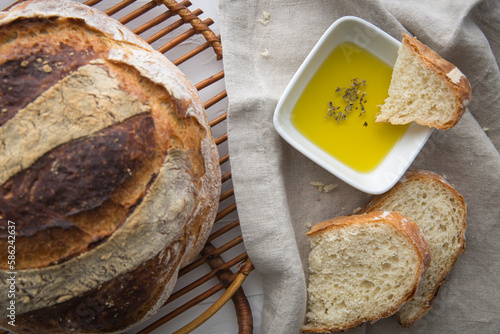 Close up of freshly baked round artisan bread, olive oil with oregano on the side which a piece pf bread dipped in.