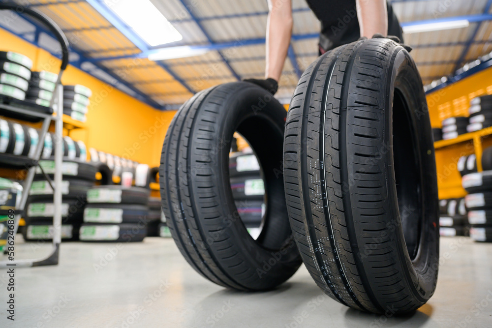 An auto mechanic at a garage or service center performing wheel changes brings new tires that are in stock in two lines to the tire shop. An auto mechanic at a garage or service center performing wheel changes brings new tires that are in stock in two lines to the tire shop.