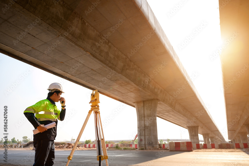 Asian male survey engineer using a theodolite in the construction of a motorway bridge Engineer working with theodolite marking concrete bridge piles at construction site