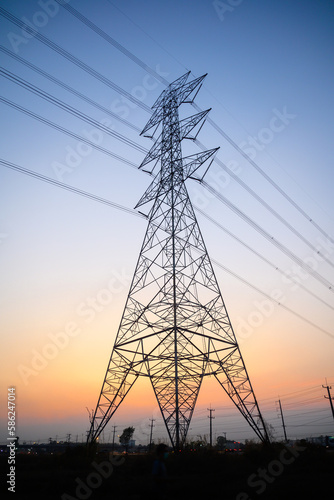Picture of a high voltage pole in the evening light at sunset. The backdrop is a beautiful orange and blue sky.
