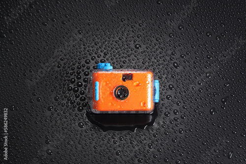 orange pocket camera or  film camera in waterproof case with water drop on black background with copy space