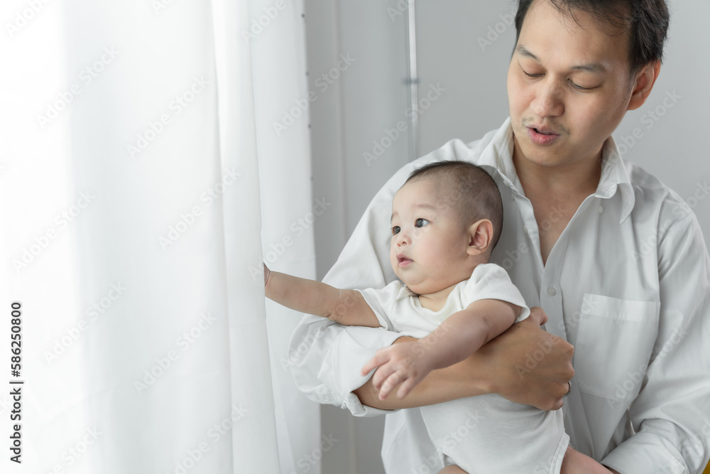 Asian young father working from home while holding his baby boy and smiling while making a break from his work. Asian young father working from home while holding his baby boy and smiling while making a break from his work.
