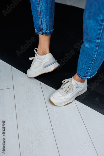 Sports shoes for women. Slender female legs in jeans and white stylish casual sneakers. Women's comfortable summer shoes. Casual women's fashion
