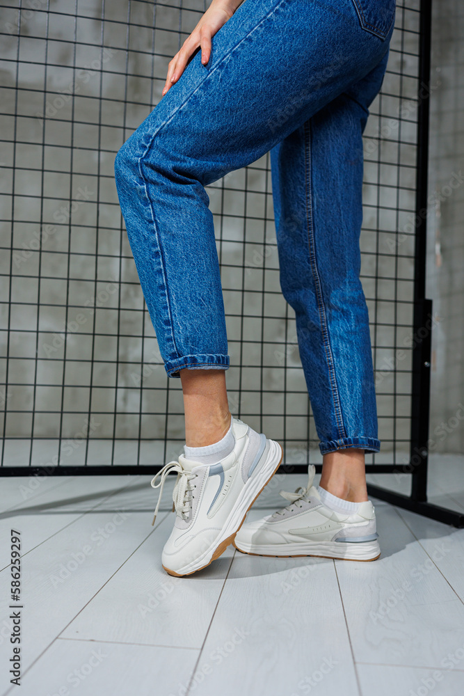 Sports shoes for women. Slender female legs in jeans and white stylish casual sneakers. Women's comfortable summer shoes. Casual women's fashion Sports shoes for women. Slender female legs in jeans and white stylish casual sneakers. Women's comfortable summer shoes. Casual women's fashion