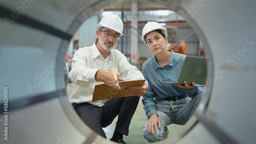 Two engineer manager leader and woman assistant holding laptop wearing helmet sitting at manufacturing factory discussing and explaining detail talking and checking production in workplace area