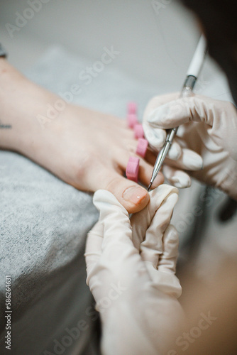 A pedicure master cleans and paints the toenails of a young girl who came to a beauty salon to take care of her feet