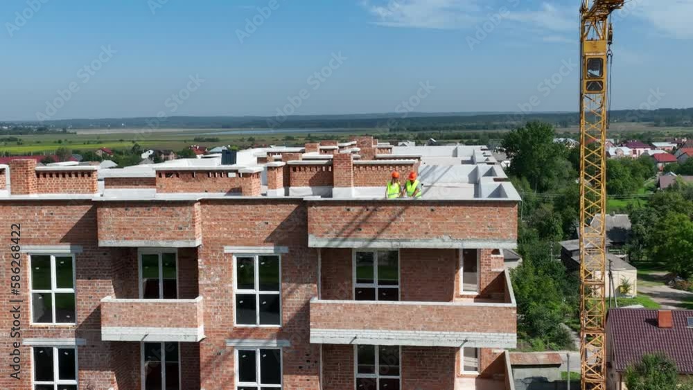 Aerial view A Builder And An Architect On The Roof Of A Brick House Inspect The Construction Plan Aerial view A Builder And An Architect On The Roof Of A Brick House Inspect The Construction Plan