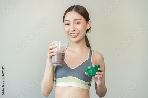 Diet meal replacement for weight loss, smile asian young woman, girl in sportswear, hand in holding protein shake bottle for drink supplement for muscle after workout at home. Healthy body care person