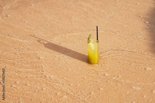 Image of a refreshing lemonade on the sand by the sea. Picture of cocktail among the waves by the sea at the beach. Visual evocative of a summer vacation trip in a tropical location.