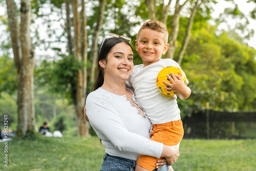 Fotografie beautiful latina girl holding her son, while the boy holds a ball in his hands