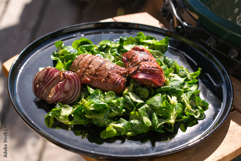ready to eat - lamb's lettuce, red onions and roasted meat from a red deer calf on a black plate