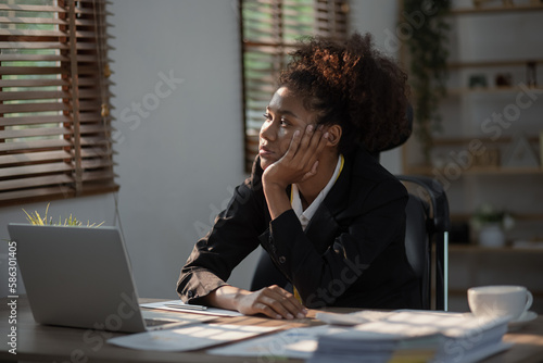 Young African American businesswoman working on laptop with documents and stressed over worked from work in the office, Overworked woman concept.