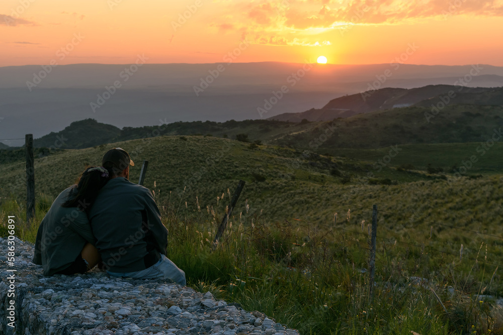 Fototapeta premium Pareja enamorada mirando el atardecer en la montaña. Sensación de libertad, calma y armonía. 