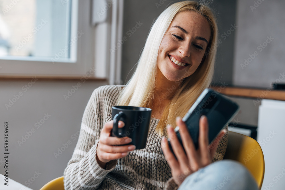 A cheerful pretty woman sits alone at home and uses her smartphone A cheerful pretty woman sits alone at home and uses her smartphone