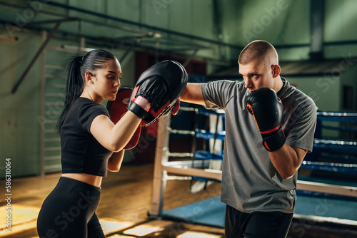 A woman holds pads while a man practices punching