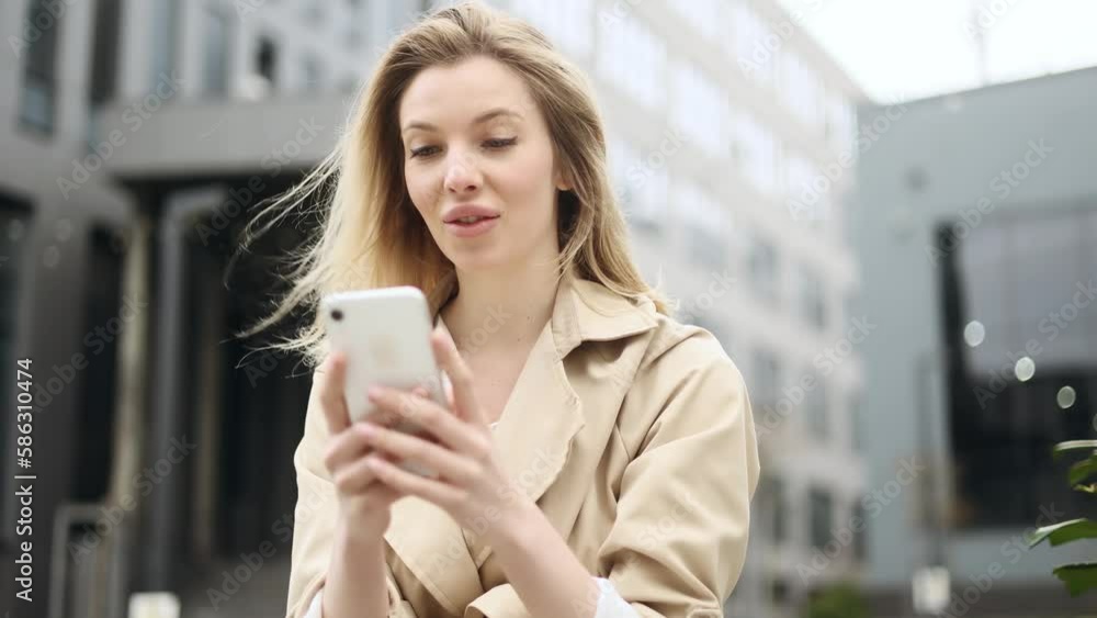 Portrait of young blond woman looking at smartphone cellphone screen with nod of approval and looking at camera pointing at the phone near business centre Advise Approve Recommend Choice concept Portrait of young blond woman looking at smartphone cellphone screen with nod of approval and looking at camera pointing at the phone near business centre Advise Approve Recommend Choice concept