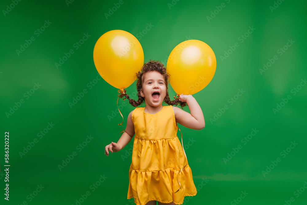 Funny little girl on a green background. A girl is having fun with yellow balloons. balloons lift up the pigtails of the child. Funny little girl on a green background. A girl is having fun with yellow balloons. balloons lift up the pigtails of the child.