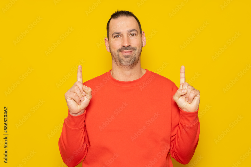 Handsome hispanic man with a beard wearing a red sweater pointing up with his fingers, isolated over yellow background Handsome hispanic man with a beard wearing a red sweater pointing up with his fingers, isolated over yellow background