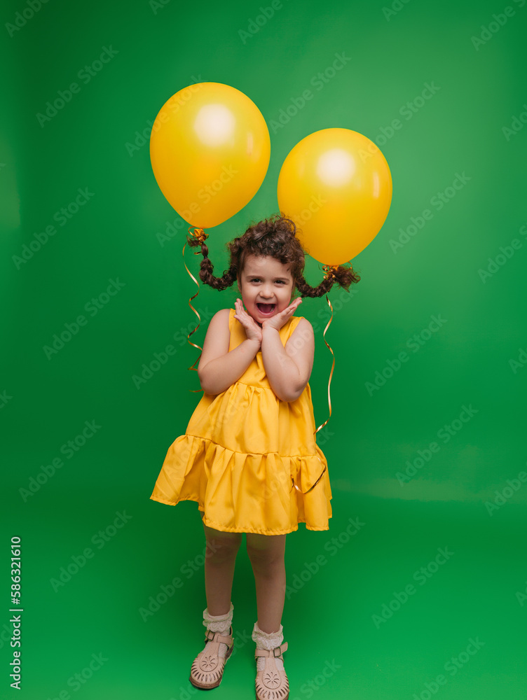 Funny little girl on a green background. A girl is having fun with yellow balloons. balloons lift up the pigtails of the child. Funny little girl on a green background. A girl is having fun with yellow balloons. balloons lift up the pigtails of the child.