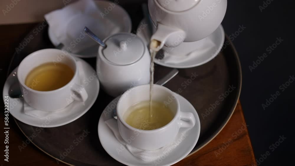 Close-up male hand pouring green herbal tea in cups from teapot. Unrecognizable professional waiter serving hot drink in restaurant cafe indoors Close-up male hand pouring green herbal tea in cups from teapot. Unrecognizable professional waiter serving hot drink in restaurant cafe indoors