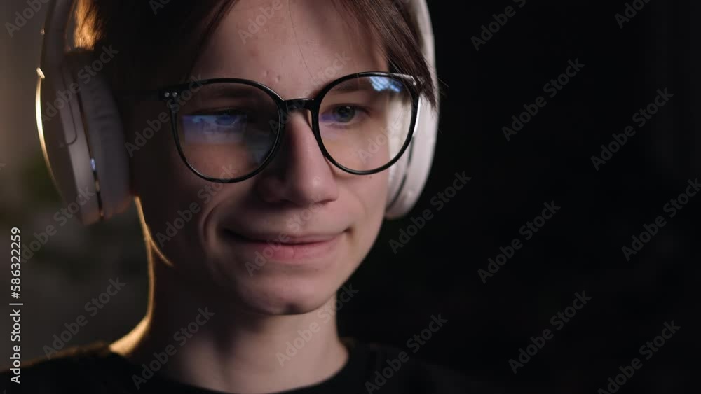 Young gamer man in glasses with screen reflection and headphones streaming live action game while explaining gameplay to subscribers. Gaming, esports, internet and virtual games at dark room. Young gamer man in glasses with screen reflection and headphones streaming live action game while explaining gameplay to subscribers. Gaming, esports, internet and virtual games at dark room.