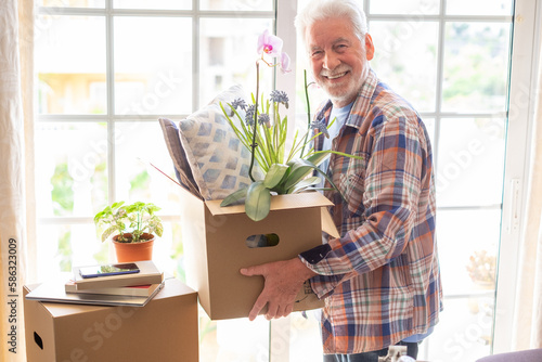 Fotografi Smiling handsome senior man holding cardboard box posing in new house in moving