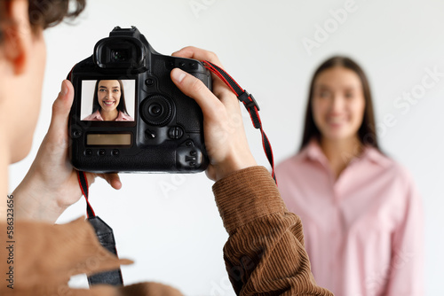 Photographer taking portrait of young beautiful woman in photostudio, focus on working digital camera during photoshoot photo