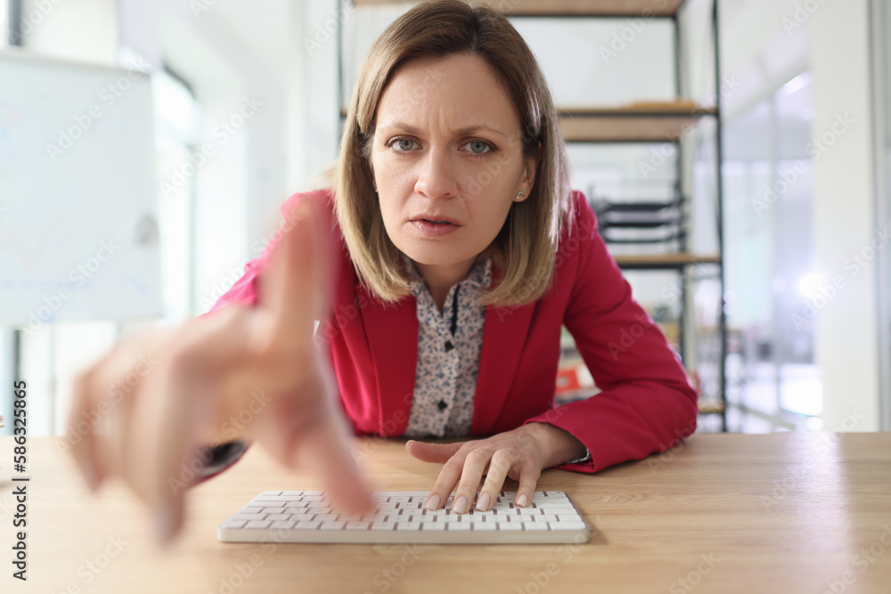 Angry woman pokes index finger at monitor typing on keyboard Angry woman pokes index finger at monitor typing on keyboard