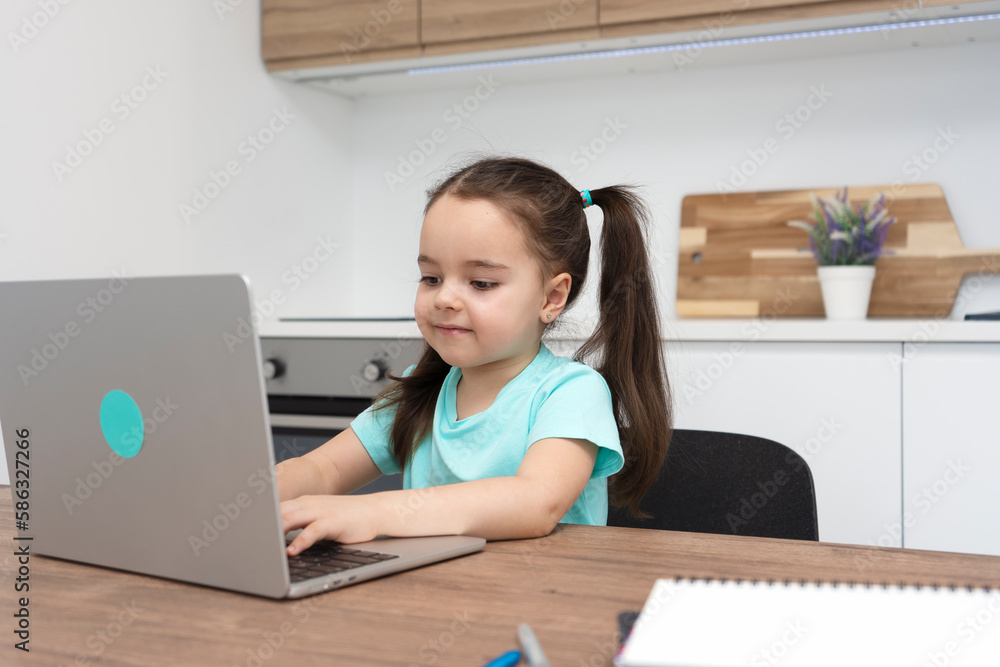 Cute little girl using a laptop, studying online at home, typing on keyboard. Cute little girl using a laptop, studying online at home, typing on keyboard.