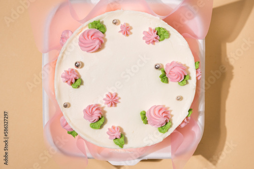 Small Korean style trendy bento cake decorated with pink cream cheese flowers in a white gift box on the beige background. Cake as a gift for a beloved one. Spring tender cake for a woman. Top view