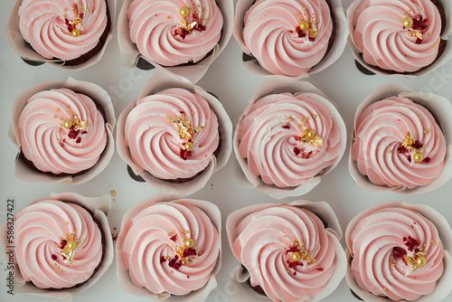 Set of cupcakes with pink whipped cream top decorated with edible golden petals and red dried berries. Close-up shot of cupcakes in the white background. Top view