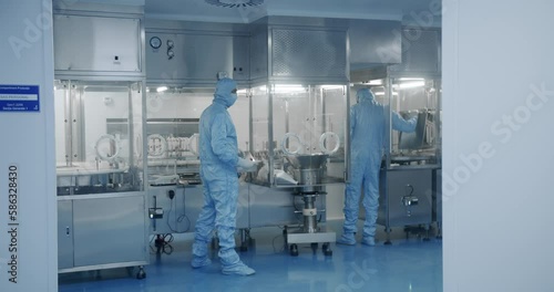 Sterile Pharmaceutical Manufacturing Laboratory where Scientists in Protective Coveralls. Factory Cleanroom. Pharmaceutical, Biotechnological and Semiconductor Creating Manufacturing Process.