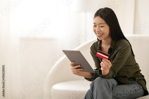Smiling asian woman using tablet and bank card at home