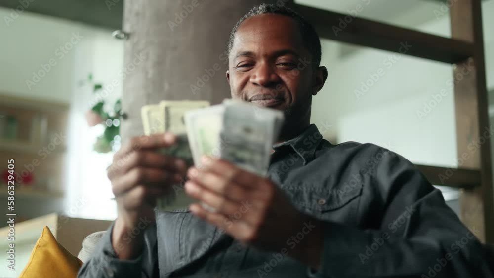 Portrait of mature african american man counting stack of dollars banknotes at home alone Successful male holding money show to camera and rejoices at good earnings income salary indoors Portrait of mature african american man counting stack of dollars banknotes at home alone Successful male holding money show to camera and rejoices at good earnings income salary indoors