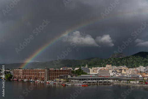 Port Louis, Mauritius - March 2023, a rainbow in front of dark grey rainy sky arises from old historic buildings in the harbor of Port Louis 